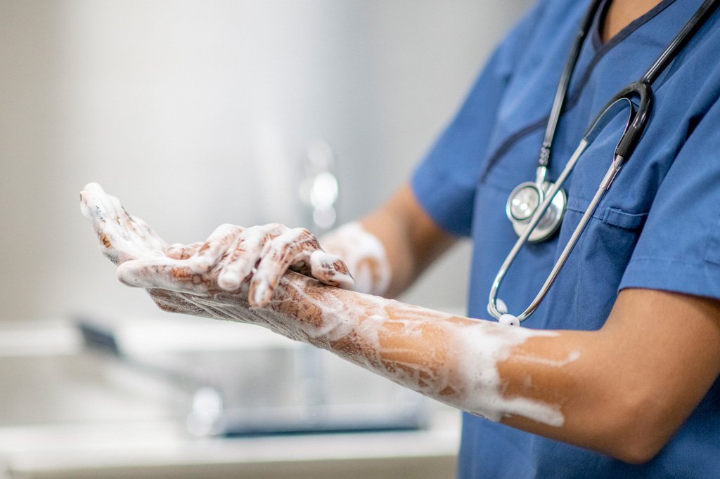 A close up photo of a person in scrubs thoroughly washing their hands and forearms. 