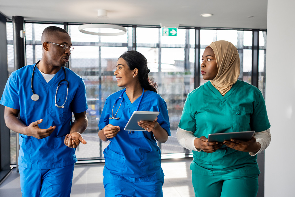 A trio of medical professionals wearing scrubs walk and talk in a medical facility corridor