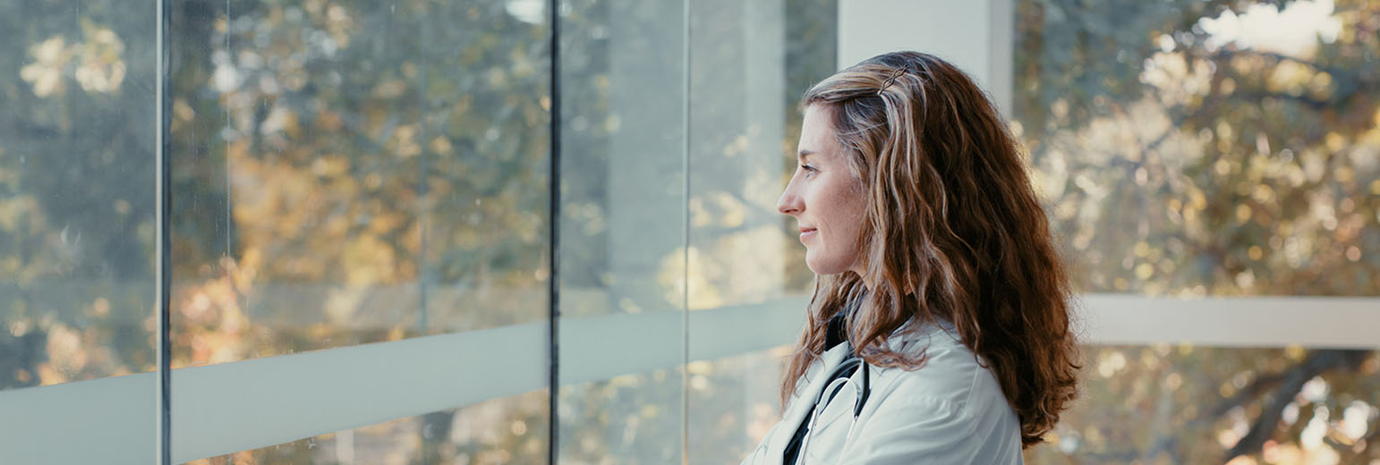 Female doctor looking out a window at nature.