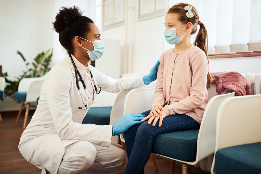 A female physician in a white coat placing her hand on a young female patient's shoulder.