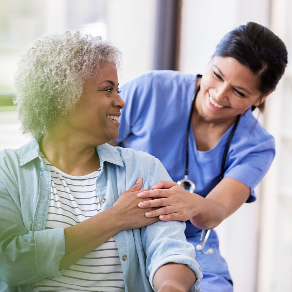 An elderly woman in a wheelchair is helped by a friendly nurse